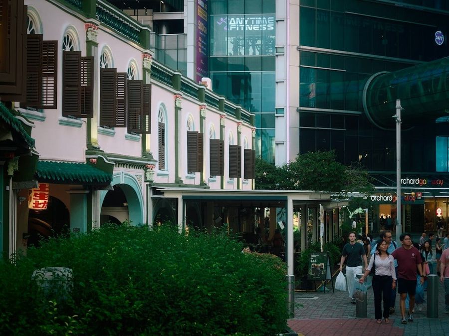 People walking past historic shophouses and a modern glass building at dusk