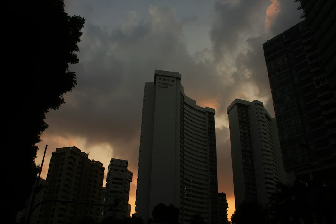 Cairnhill Plaza apartment towers silhouetted against a dark cloudy sky at low sun